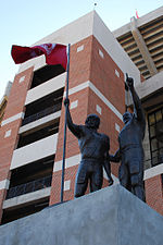 Two bronze statues of American football players holding a flag with a stadium visible at rear.