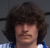 A mustached person with dark hair looking toward the camera