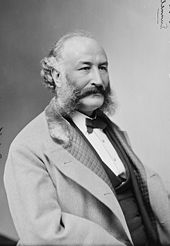 Back and white photo of a bearded man wearing a suit and a bow tie looking right