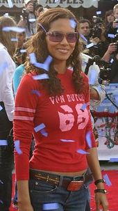 Upper body shot of Berry in long sleeved red jersey and jeans with midriff slightly exposed. A crowd in is the background.