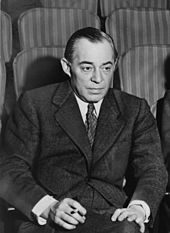 Photo of Rodgers, in middle age, seated in a theatre, wearing a suit and holding a cigarette