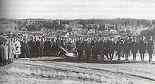 A crowd of men gathered in a field watching one man push a plow