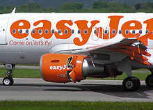 The middle of an airplane fuselage, white with "easyJet" painted in orange, is visible with the jet engine under the wing in the center of the image. Small doors on the rear half engine are open.