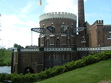 Round brick building of gothic architecture with steel beams protruding from the windows