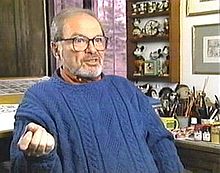 Man approximately sixty years old, with a graying beard and mustache, wearing large glasses and a bright blue sweater.