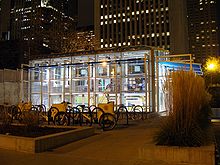 Rows of outdoor bike racks in a plaza in front of an interior-illuminated glass building at night