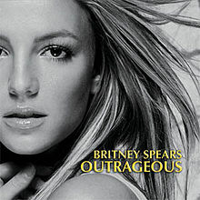 The headshot of a young blond woman. Her hair is blond and feathered straight. She is wearing lipstick and makeup. Her mouth is slightly open and her hand is pressed against her neck. In the bottom, the words "Britney Spears" are written in yellow italics. Below, the word "Outrageous" is written in the same fashion.