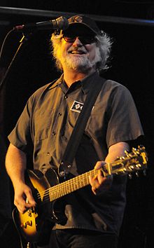 Scott McCaughey holding a guitar and smiling onstage