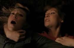 A screenshot of the episode, depicting a blond-haired woman lying on her back with her mouth open in pain, as the arm of an identical woman with red-hair is wrapped around her neck in a headlock.