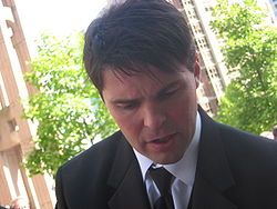 Jagr, a caucasian man with short, brown hair, has his head turned down slightly and is wearing a black suit and tie with a white dress shirt.