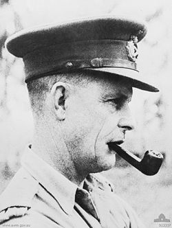 Black and white side-bust photo of a man dressed in a military uniform. He is wearing a hat while smoking a pipe.