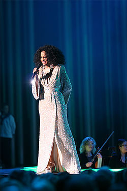 A woman in a long white coat singing into a microphone.