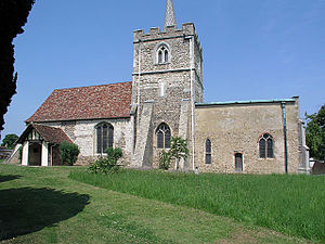 A stone church seen from the south, with a central battlemented tower, the nave with a porch and red tiled roof to the left, and a smaller chancel with a flat copper roof to the right