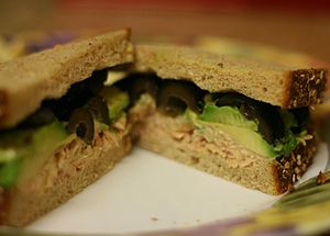 A tuna fish sandwich with black olives and avocado