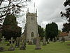 Stone church tower with flag pole. In the foreground are gravestones on grass.