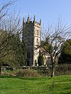 Stone building with prominent square tower. Surrounded by trees and wth green grass area in the foreground separated from the building by a stone wall.