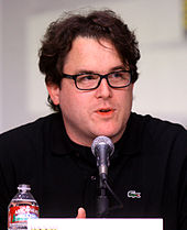 A headshot of a dark-haired man, wearing glasses and opening his mouth to speak