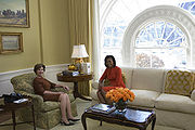 Another woman sits in a stuffed chair, and Michelle Obama sits on an adjacent couch.