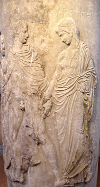A carving of a noble robed man and woman apparently leading a demure, robed woman. The man's robe is open, exposing his penis. He holds the hand of the woman.
