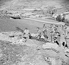 Six men around an artillery gun dug in with another gun in the distance