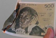 Banknote held by thumb and forefinger; smoldering on the opposite side