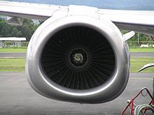A zoomed-in view of the front of an engine nacelle. The fan blades of the engine are in the middle of the image. They are surrounded by the engine nacelle, which is seemingly circular on the top half, and flattened on the bottom half.