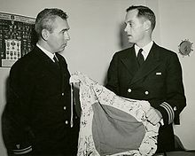 Two men in uniform, one holding a flag.