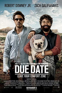 A man in a ragged blue shirt with his wrist in a cast, and his arm around a smiling bearded man holding a bulldog that is wearing a protective cone around its neck.