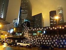 After dark, hundreds of silver stars on the walls. In front of tall buildings downtown, cars parked in front.