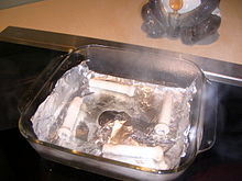 Aluminum foil in a square Pyrex dish of water, with a tear where the foil has melted