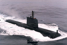 A black submarine travelling on the surface of the sea
