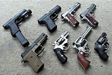 A collection of eight different handguns resting on the ground