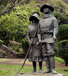 Photo displaying one male and one female bronze figure both wearing hats