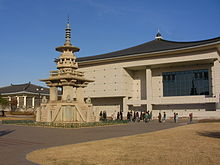 A model of a stone pagoda on the left and an ivory building with a cursive dark blue roof on the background