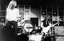 A black and white photograph of Robert Plant performing with microphone stand and Jimmy Page with guitar