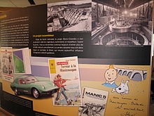 An exhibit illustrating the impact of the Manic-Outardes hydroelectric project with a car, a Hergé drawing of Tintin, a paperback, a picture of a man filming an action scene, a videocassette box, a stamp and a sports car.