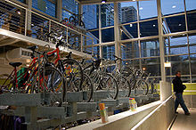 Side view of bikes parked in indoor bike racks, with tall windows beyond the racks