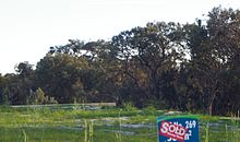 a grassed area in the foreground with a 'sold' real estate sign, against a background of banksia woodland