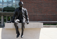 Photo of a statue of Neil Armstrong sitting on a ledge. The words "Neil Armstrong Hall of Engineering" are visible on the building in the background.