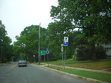 A two lane undivided road in a wooded residential area with roadside signs reading south Route 54, Atlantic City Expressway straight, and a green sign reading Route 54 south Buena straight
