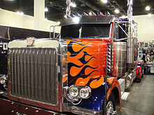 A Peterbilt 379 truck is seen at BotCon 2011, it is beside a promotional poster of the film, with people behind the truck.