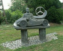 A bust of Caracciola sits behind a statue of a single-seater racing car; the Mercedes three pointed-star is beside that.