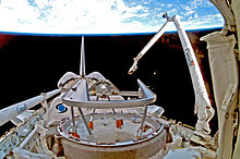 A shuttle in space, with Earth in the background. A mechanical arm labeled "Canada" rises from the shuttle