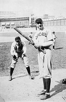 Two men in baseball uniforms bearing the word "Chicago" on the chest—one is bent over prepared to catch a pitched ball, the other stands ready to swing a baseball bat.