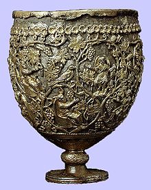 A photo of a large ovoid vessel standing on a short knobbed stem. The cup comprises a silver body enclosed in an openwork layer of gold. The gold ornamentation represents vine scrolls enclosing small seated and praying figures.