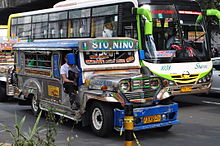 Blue and white jeepney with a green and white bus behind it