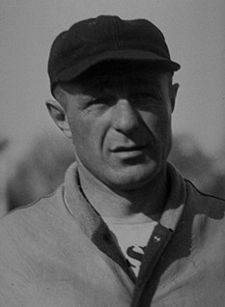 Head-and-shoulders photo of Charlie Bachman, white man in his late 40s, shown in baseball cap and pullover sweater unbuttoned at the neck.