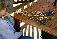 Seated boy facing 3/4 away from camera, looking at a ball-and-stick model of a molecular structure. The model is made of colored magnets and steel balls.
