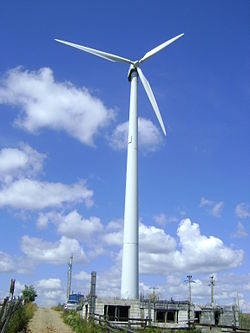 A wind turbine standing on a field next to a small hut