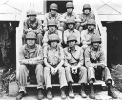 Black-and-white photo of eleven Marines in their combat uniforms sitting on some stairs